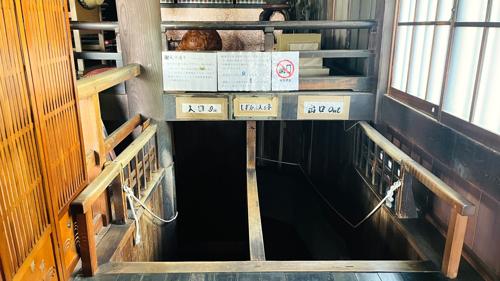 戒壇巡りの入口。「入口」「出口」の札と、暗がりへ降りていく木の階段