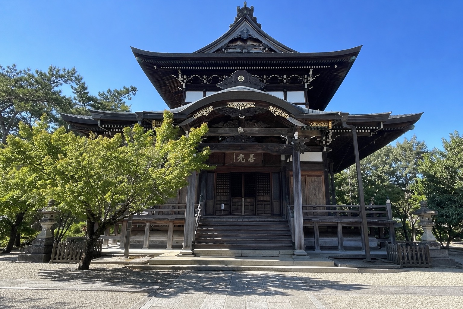 関善光寺 本堂（大仏殿）の全景。青空に金の装飾と「善光」の扁額が映える